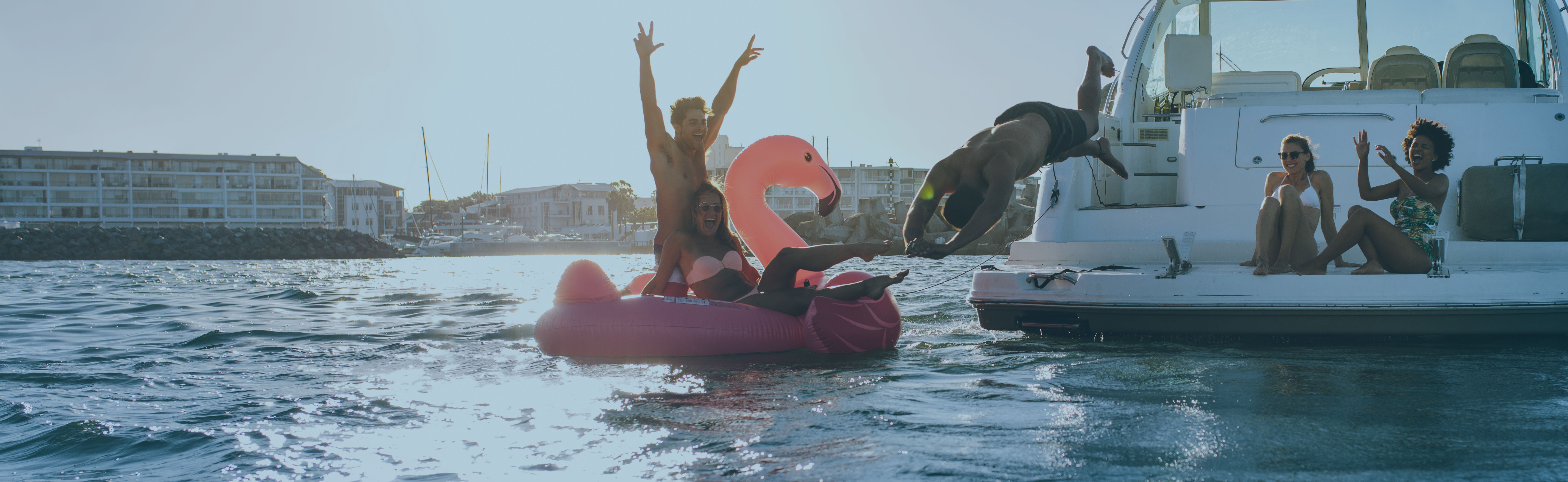 Freunde springen und plantschen auf einem aufblasbaren Flamingo vom Boot ins Wasser