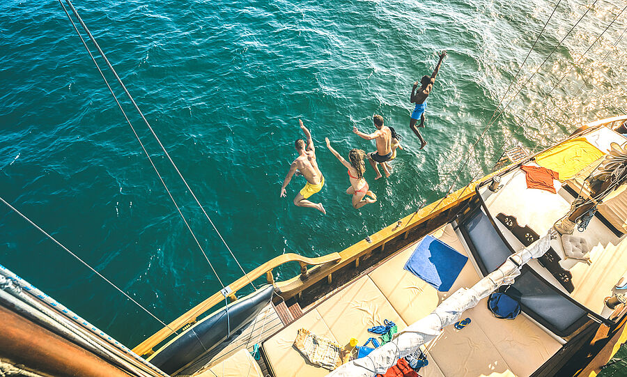 Blick von oben: Crew springt nacheinander von der Yacht ins Meer