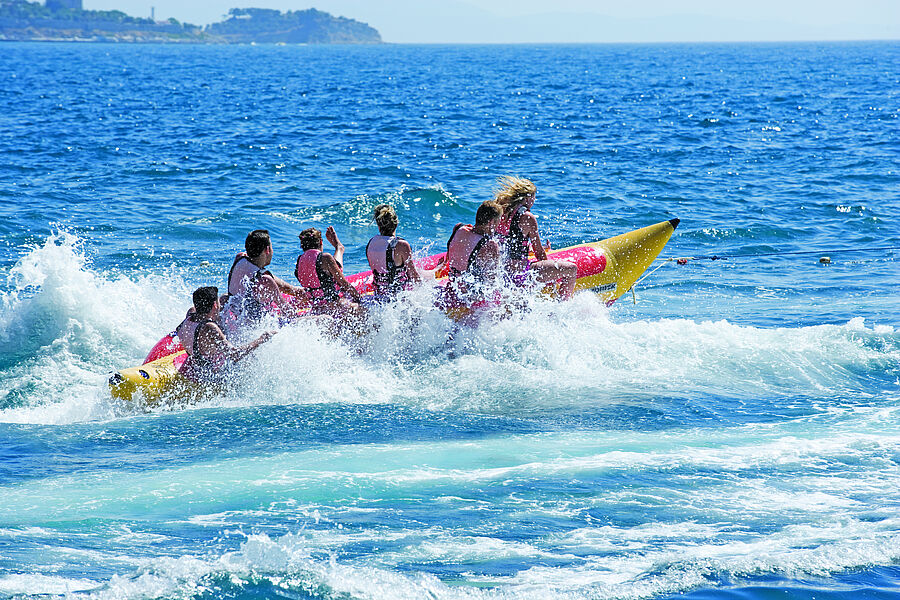 Gruppe fährt lachend auf einem Bananenboot durch die Wellen