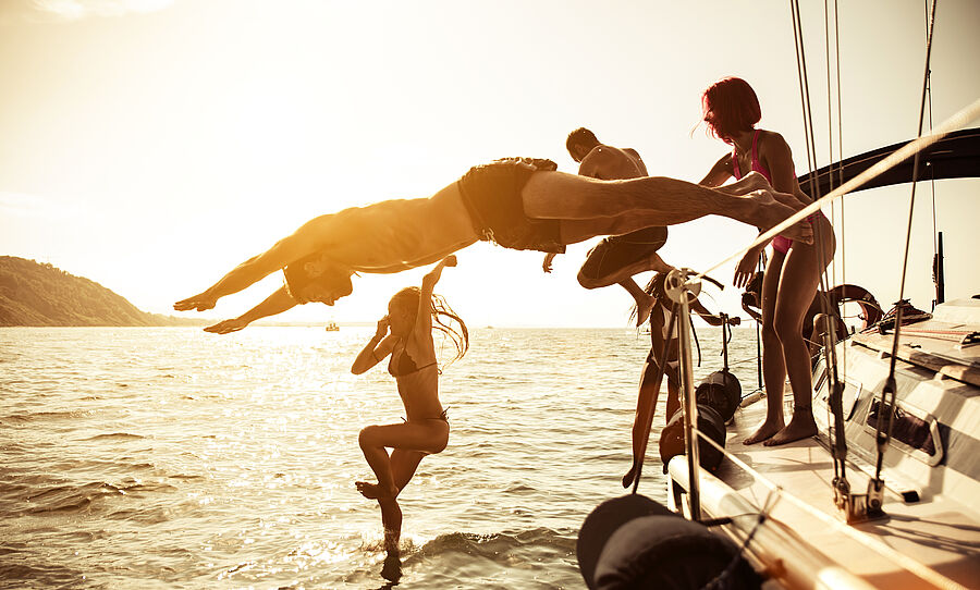 Freunde springen bei Sonnenuntergang von der Yacht ins Wasser