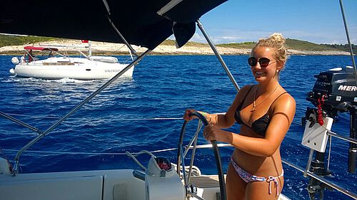 Crew-Mitglied steuert die Yacht, im Hintergrund ein weiterer Katamaran